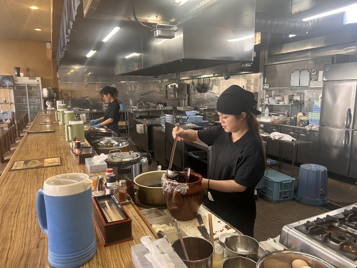 立ちのぼる湯気、炒め野菜の香ばしさ。あたたかい一杯を仲間と届けるオープンキッチン。